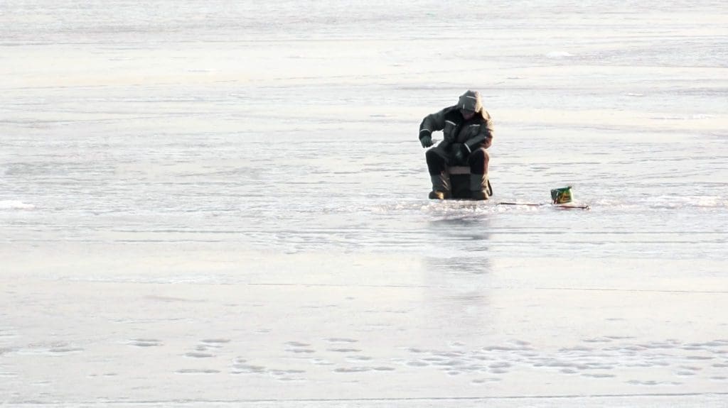 man sitting on a cooler ice fishing on a lake